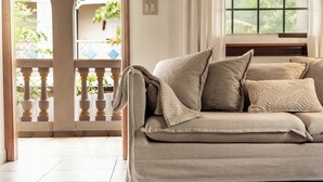 A beige sofa with a throw blanket and patterned pillows in a room with a tiled floor and a view of a balcony with plants. - 2 Bedroom Tropical Bliss Villa • Unbeatable Views in Mont Vernon (Mont Vernon)