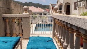 En balkon med swimmingpool, hvide gelændere og blå puder.
