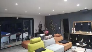 Un salon moderne avec un canapé, une table basse et un téléviseur. Une porte vitrée donne accès à un coin repas.