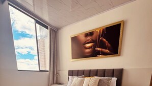 Ein Schlafzimmer mit einem großen Bett, einem Fenster mit Blick zum Himmel und einem gerahmten Kunstwerk an der Wand.