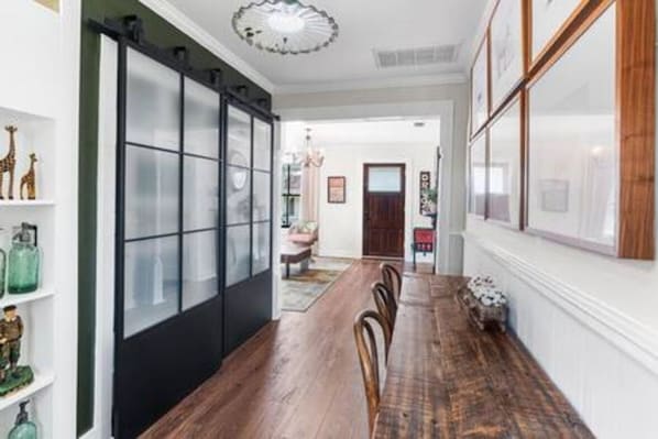 A dining area with a long wooden table, chairs, and a black sliding door with frosted glass panels.
