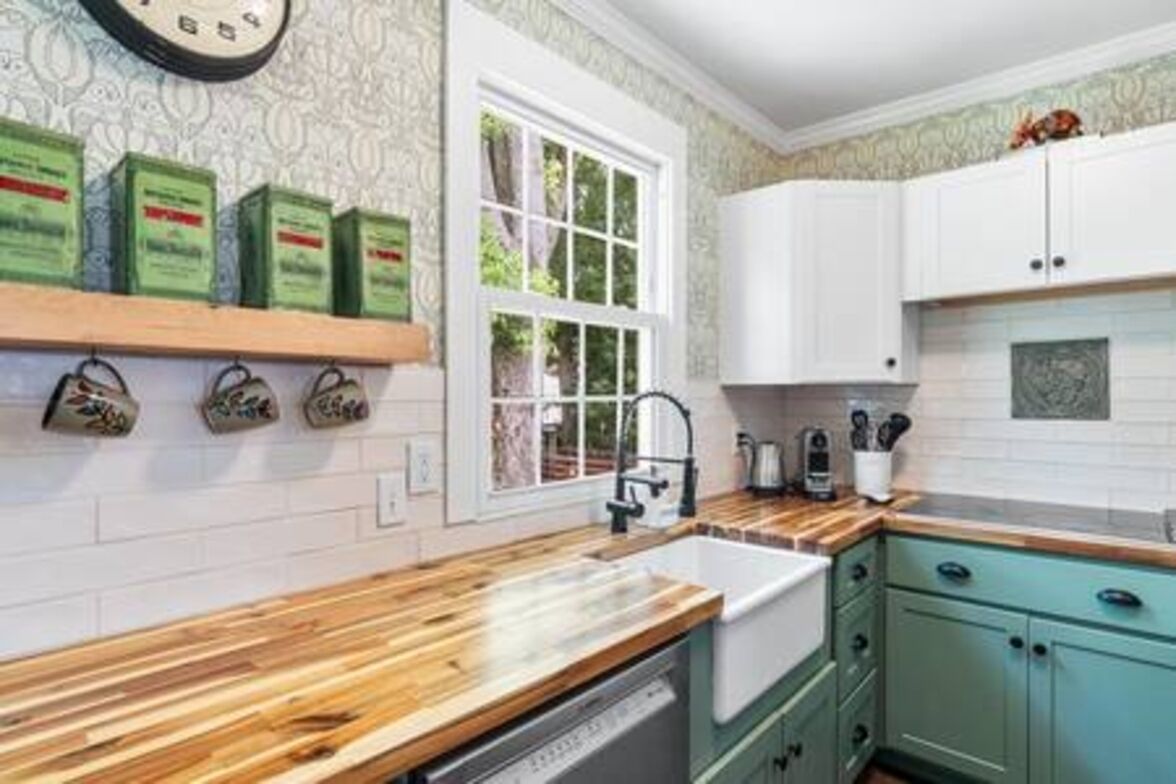 Een keuken met witte kastjes, een houten aanrecht en een raam met uitzicht op groen.