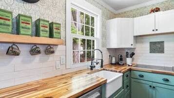 Een keuken met witte kastjes, een houten aanrecht en een raam met uitzicht op groen.