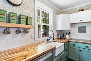 A kitchen with white cabinets, a wooden countertop, and a window with a view of greenery.