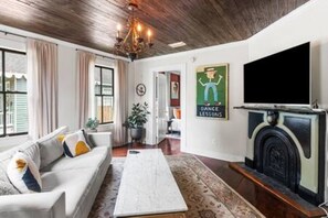 A living room with a sofa, a coffee table, a fireplace, a television, and a wall with a poster.