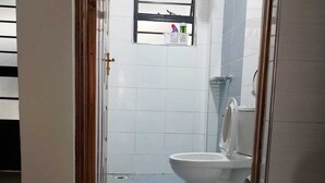 Ein Badezimmer mit Toilette, kleinem Fenster und Duschkopf.