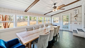 Un espace repas avec une table et des chaises en bois, de grandes fenêtres et un ventilateur de plafond.