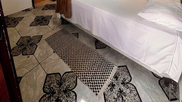 A hotel room with a bed, a TV mounted on the wall, a small kitchenette, and a bathroom visible through an open door. - Casa Brisa Noronha (Fernando de Noronha)