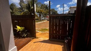 An open wooden door leading to a paved area with a view of palm trees and a clear sky. - Casa Brisa Noronha (Fernando de Noronha)