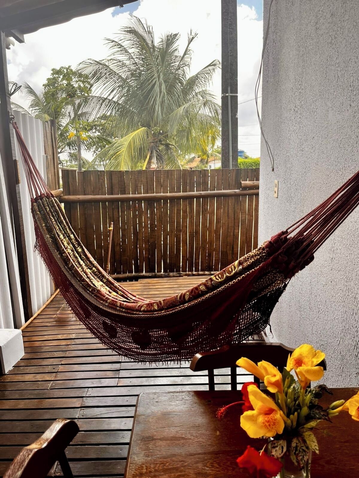 Una silla hamaca sobre una terraza de madera con vistas a palmeras y una valla de madera.