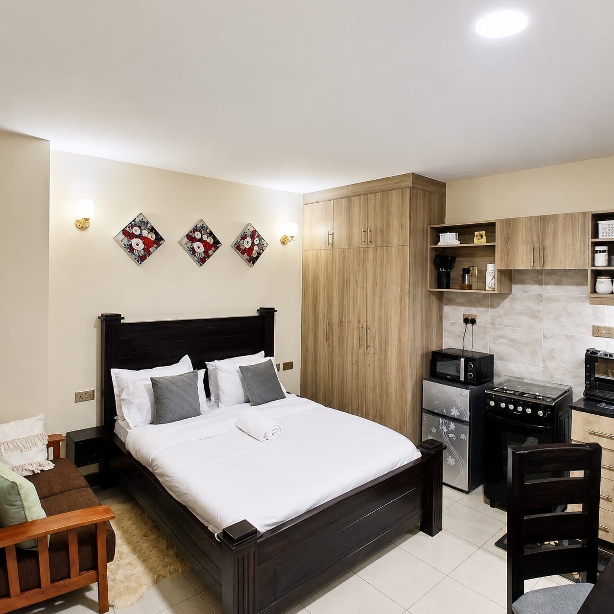 Quarto com cama, mesas de cabeceira, uma cadeira e uma cozinha compacta com micro-ondas e fogão.