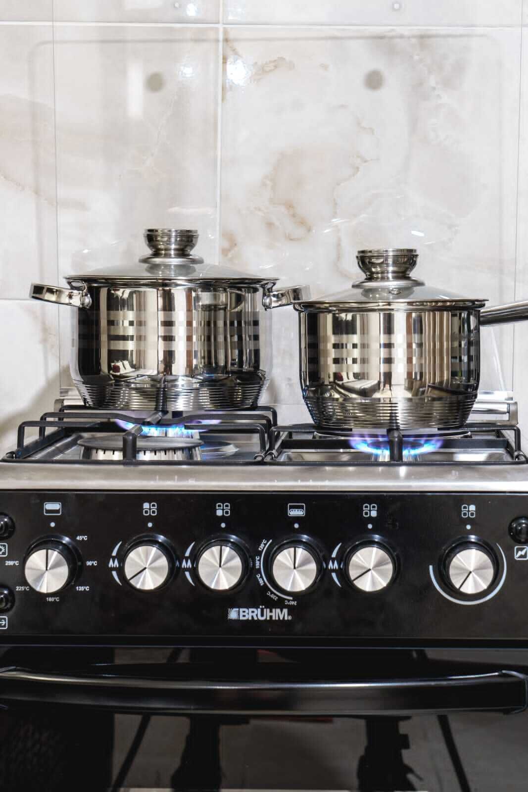 A kitchen with two stainless steel pots on a gas stove, a control panel with temperature settings, and a tiled backsplash.