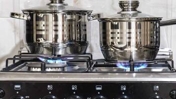 A kitchen with two stainless steel pots on a gas stove, a control panel with temperature settings, and a tiled backsplash.