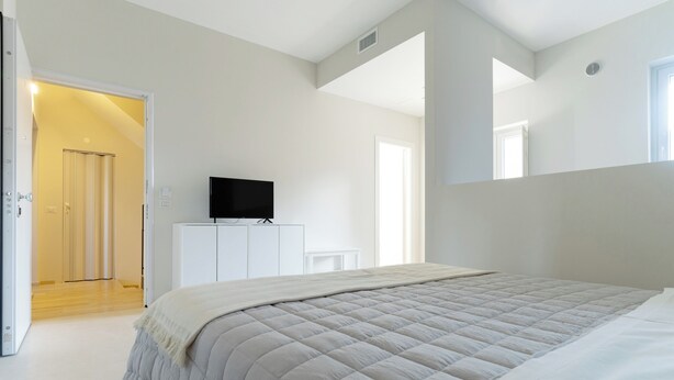 Un dormitorio con una cama grande, un televisor sobre un mueble bajo y una puerta que da a otra habitación.