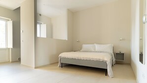 Un dormitorio amplio con una cama grande, una mesita de noche y otra mesita auxiliar.