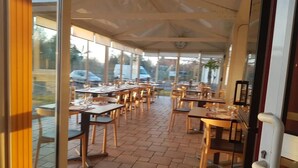 An outdoor dining area with tables and chairs, a tiled floor, and a covered section with a clock. - Havana (Malay-le-Grand)