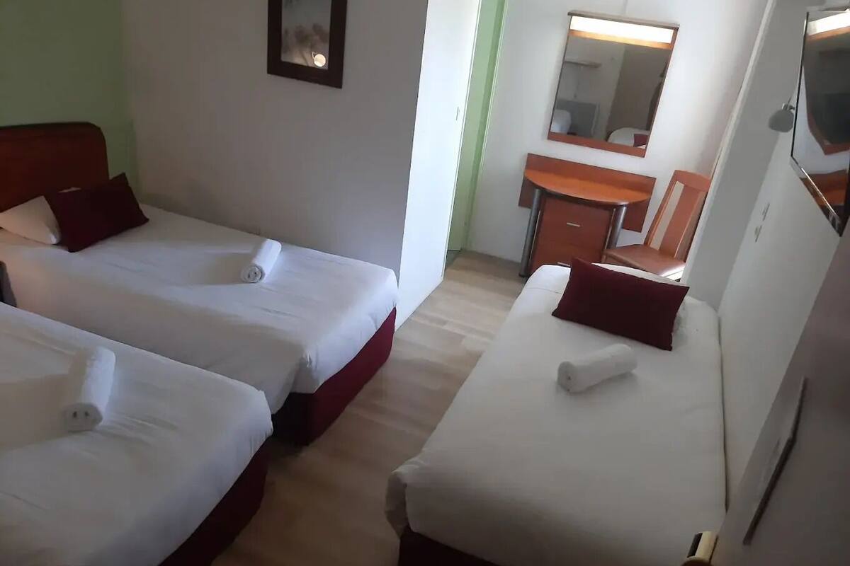 Ein Hotelzimmer mit zwei Einzelbetten, einem Schreibtisch, einem Stuhl und einem Spiegel.
