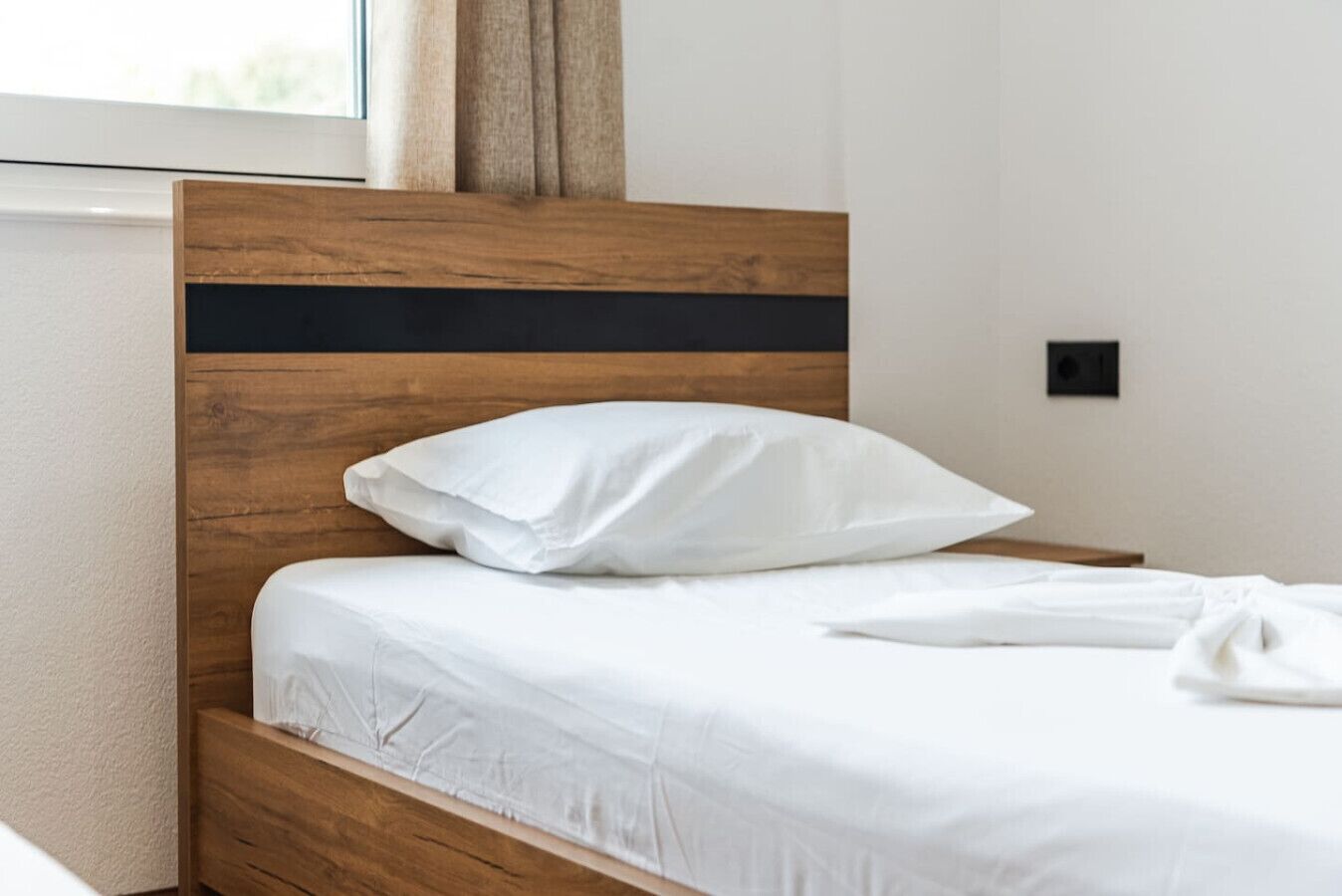 A neatly made bed with white linens and a wooden headboard.
