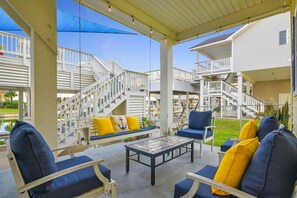 A covered outdoor seating area with a swing set, a table, and chairs with cushions.