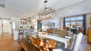 A spacious living area with a glass dining table, a wooden coffee table, and a modern chandelier. - Upscale Waterfront Boat Lift~Kayaks~Pets~Sleeps12 (Galveston)