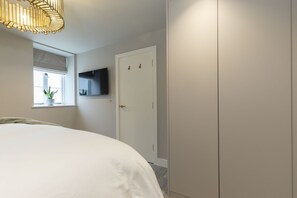 A bedroom with a bed, a window with a plant, a TV on the wall, and a wardrobe. - Luxury 1-Bed Annex on Rodborough Common (Rodborough Common)