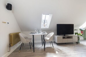 A modern, well-lit room with a dining table set for four, a flat-screen TV, and a skylight.