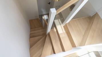 A wooden staircase with white handrails and a glass railing, leading to a room with a white door and a hanging light fixture.