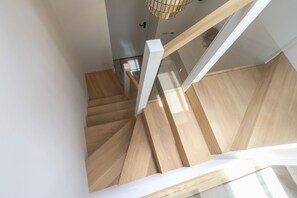 A wooden staircase with white handrails and a glass railing, leading to a room with a white door and a hanging light fixture. - Luxury 1-Bed Annex on Rodborough Common (Rodborough Common)