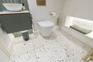 A modern bathroom with a white toilet, a sink with a large bowl, a trash can, and a towel rack.