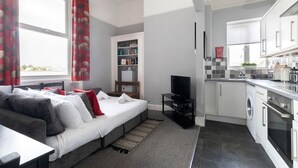 A modern apartment with a sofa bed, a TV, a kitchen with appliances, and a laundry area.