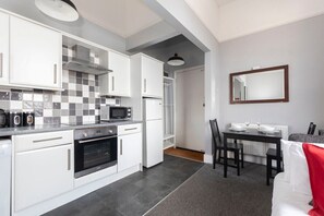 A compact kitchen with white cabinets, a microwave, an oven, and a dining area with a table and chairs.