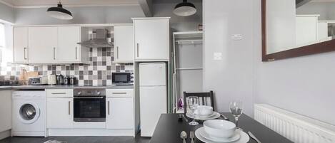 Une cuisine moderne avec des meubles blancs, un four à micro-ondes, un lave-linge et un coin repas avec une table dressée pour deux personnes.