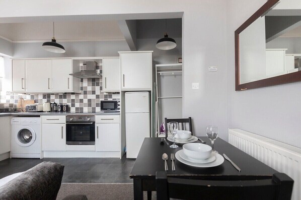A modern kitchen with white cabinets, a microwave, a washing machine, and a dining area with a table set for two.