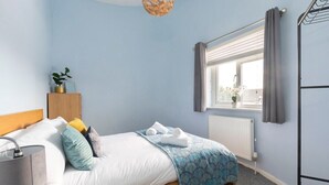 A bedroom with a bed, a bedside table with a lamp, a window with curtains, and a radiator.