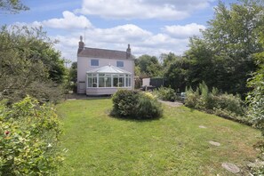 A house with a conservatory, surrounded by a well-maintained garden with various plants and a lawn.