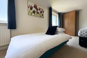 Une chambre avec un lit simple, une armoire en bois, une fenêtre avec des rideaux et un tableau floral accroché au mur.