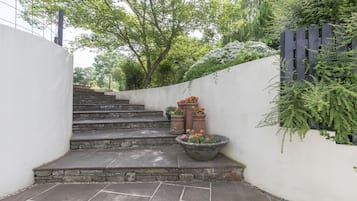 A set of stone steps leading up to a white wall with a wooden fence and greenery.