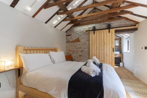 Une chambre à coucher avec un lit en bois, du linge de lit blanc, un mur en pierre et un plafond en bois.