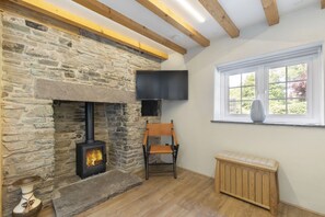 A cozy room with a stone fireplace, a wooden bench, and a window with a view of greenery. - Tranquil Cottage with Hot Tub close to Offa’s Dyke (Abergavenny)
