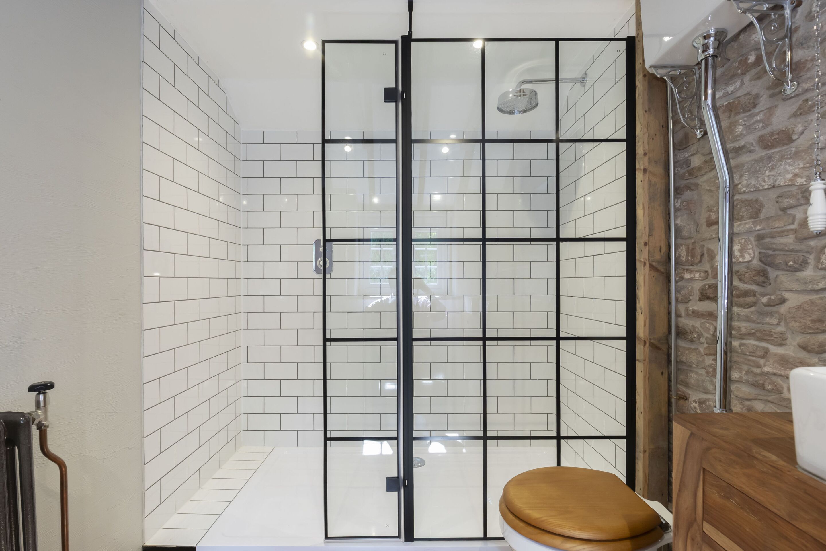 Ein modernes Badezimmer mit einer in Glas abgeschlossenen Dusche, weißen Fliesen und einem Holzkosmetikschrank.