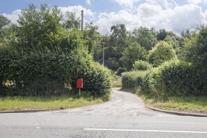 A rural road with a red mailbox on the left, surrounded by dense greenery and trees. - Tranquil Cottage with Hot Tub close to Offa’s Dyke (Abergavenny)