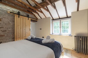 Un dormitorio con cama, vigas de madera en el techo, pared de piedra, ventana y radiador.