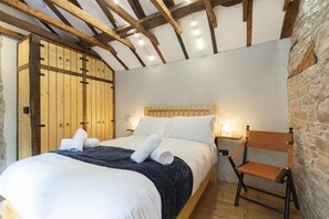Ein Schlafzimmer mit einem hölzernen Bett, weißer Bettwäsche, einer Steinsäule und einem Holzstuhl.