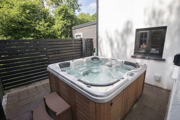 A hot tub with wooden benches, a wooden fence, and a window with a view of trees.