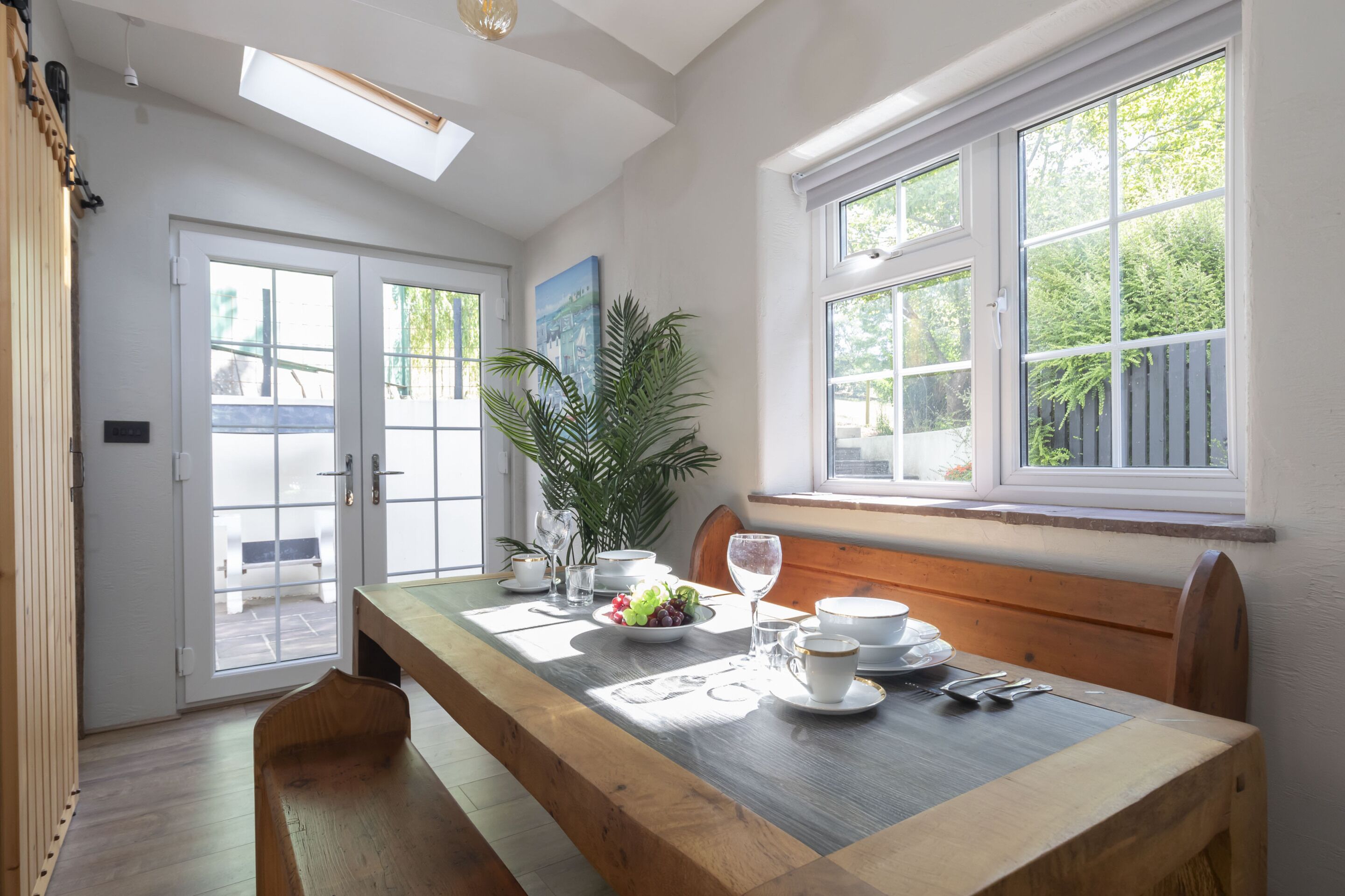 A dining area with a wooden table set for four, a bench, and a potted plant.
