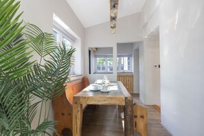Ein Essbereich mit einem Holztisch, gedeckt für vier Personen, umgeben von großen Fenstern und einem Blumentopf.