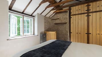 A bedroom with a large bed, wooden beams, a stone wall, and a wooden wardrobe.