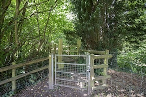 A wooden gate with a metal fence, surrounded by dense greenery and trees.