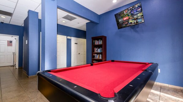A pool table with a red felt surface, surrounded by blue walls and a bookshelf. - Caribe Cove Charm - For 8! (Kissimmee)