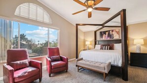 A bedroom with a four-poster bed, two armchairs, a bench, a ceiling fan, and a large window with a view. - Spacious Home in Prime Location | Pool, Spa, Games (Glendale)
